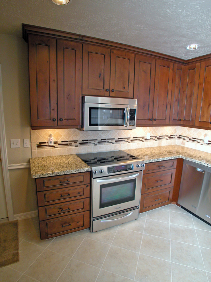 This is an example of a mid-sized traditional l-shaped eat-in kitchen in Houston with an undermount sink, recessed-panel cabinets, brown cabinets, granite benchtops, beige splashback, glass tile splashback, stainless steel appliances, ceramic floors and no island.