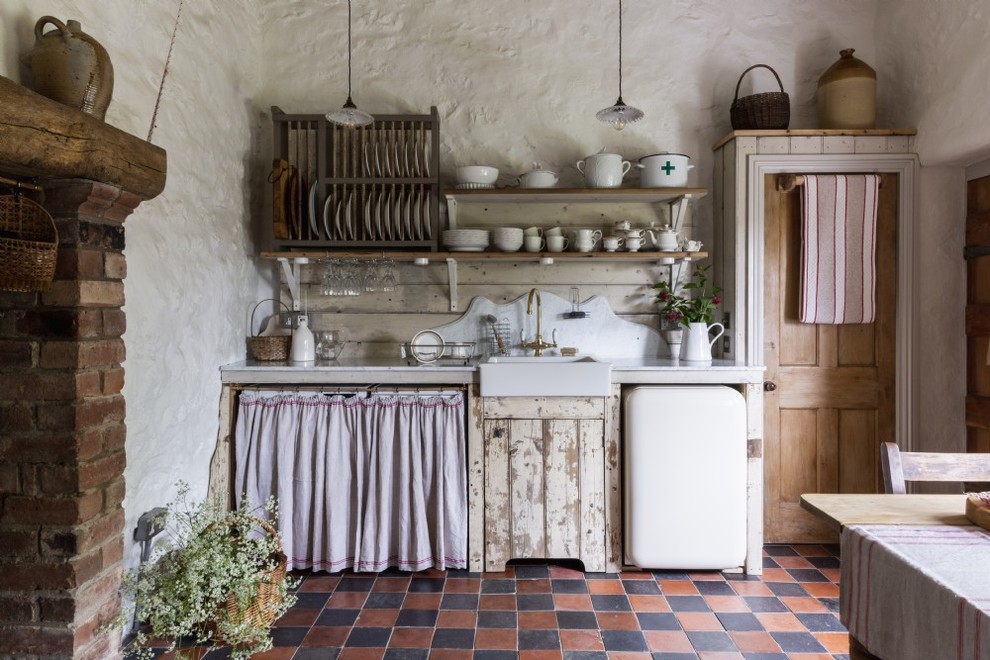 This is an example of a mid-sized country single-wall eat-in kitchen in Other with a farmhouse sink, terra-cotta floors, multi-coloured floor, open cabinets, timber splashback, no island, white benchtop and distressed cabinets.