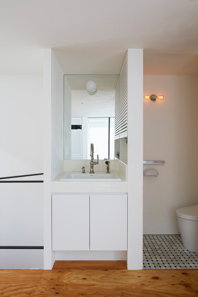 Photo of a small midcentury powder room in Tokyo with beaded inset cabinets, white cabinets, a one-piece toilet, white tile, white walls, an undermount sink, grey floor and white benchtops.