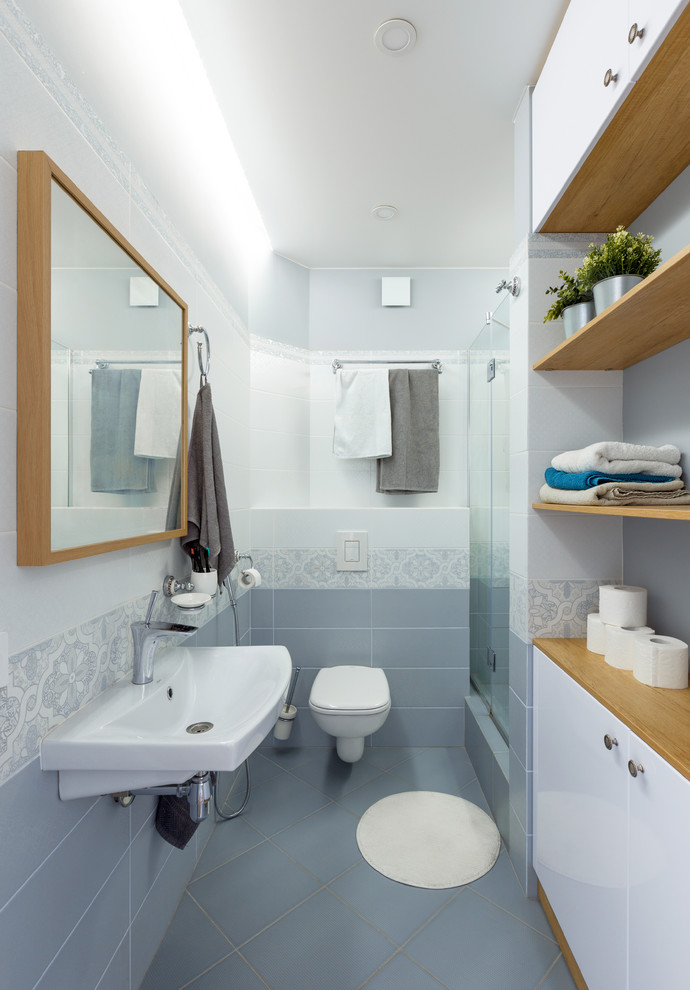 Photo of a mid-sized contemporary 3/4 bathroom in Novosibirsk with flat-panel cabinets, white cabinets, an alcove shower, a wall-mount toilet, gray tile, ceramic tile, grey walls, ceramic floors, a wall-mount sink, grey floor and a hinged shower door.