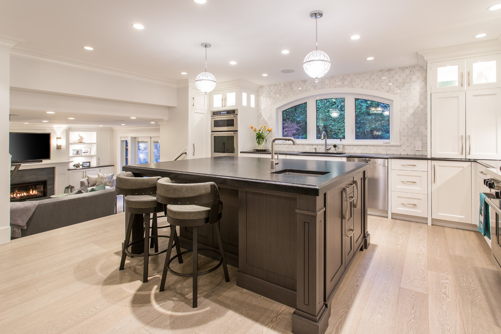 Inspiration for a large transitional l-shaped medium tone wood floor and beige floor eat-in kitchen remodel in Vancouver with an undermount sink, shaker cabinets, white cabinets, granite countertops, gray backsplash, marble backsplash, stainless steel appliances, an island and black countertops