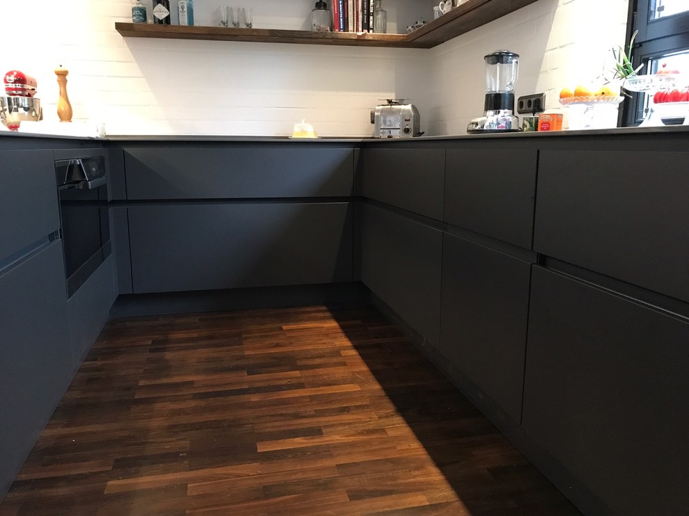 This is an example of a large industrial u-shaped eat-in kitchen in Other with an integrated sink, flat-panel cabinets, grey cabinets, quartz benchtops, white splashback, brick splashback, stainless steel appliances, dark hardwood floors, a peninsula and yellow benchtop.