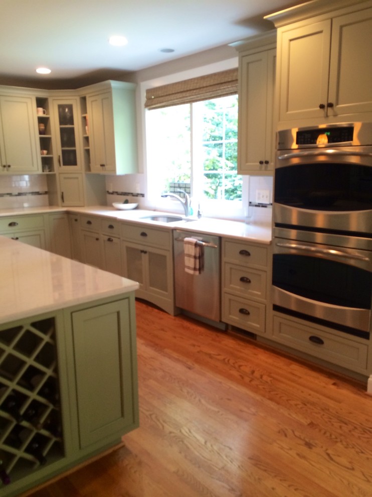 Example of a mid-sized transitional medium tone wood floor and brown floor kitchen design in DC Metro with an undermount sink, shaker cabinets, green cabinets, marble countertops, white backsplash, subway tile backsplash, stainless steel appliances and an island