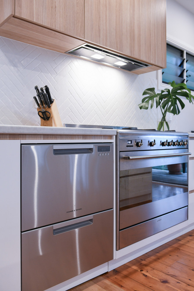 Inspiration for a large scandinavian l-shaped eat-in kitchen in Sydney with a drop-in sink, flat-panel cabinets, white cabinets, laminate benchtops, white splashback, ceramic splashback, stainless steel appliances, medium hardwood floors, with island, brown floor and grey benchtop.