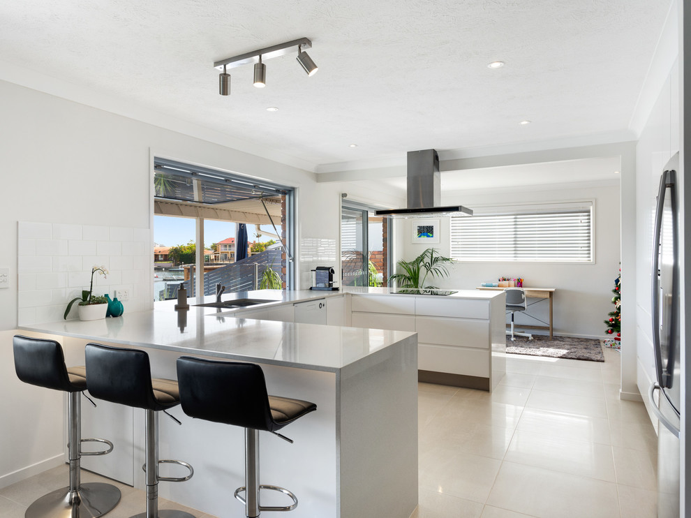 This is an example of a mid-sized modern u-shaped eat-in kitchen in Gold Coast - Tweed with an undermount sink, flat-panel cabinets, white cabinets, quartz benchtops, white splashback, subway tile splashback, white appliances, no island and white benchtop.