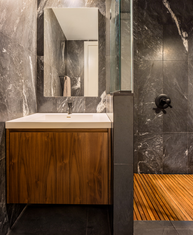 Modern bathroom in New York with flat-panel cabinets, medium wood cabinets, a corner shower, black tile, stone tile, black walls, quartzite benchtops, black floor, a hinged shower door, white benchtops and a single vanity.
