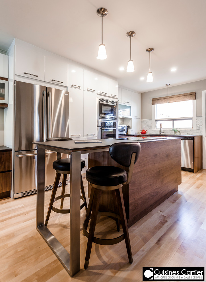 Example of a large transitional galley medium tone wood floor eat-in kitchen design in Montreal with an undermount sink, flat-panel cabinets, dark wood cabinets, quartzite countertops, white backsplash, mosaic tile backsplash, stainless steel appliances and an island