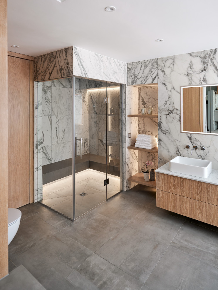 Ejemplo de cuarto de baño principal, doble y flotante contemporáneo grande con armarios con paneles lisos, puertas de armario de madera clara, bañera exenta, ducha abierta, sanitario de pared, baldosas y/o azulejos grises, baldosas y/o azulejos de mármol, paredes multicolor, suelo de baldosas de cerámica, lavabo con pedestal, suelo gris y ducha con puerta con bisagras