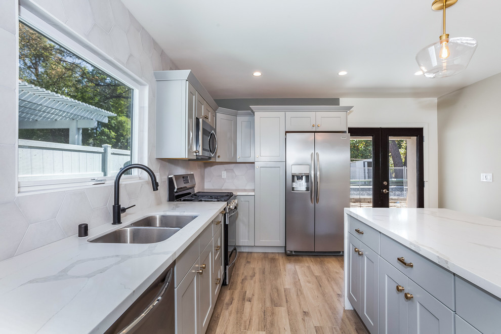 Inspiration for a mid-sized contemporary l-shaped eat-in kitchen in Los Angeles with an undermount sink, shaker cabinets, grey cabinets, quartz benchtops, grey splashback, porcelain splashback, stainless steel appliances, vinyl floors, with island and brown floor.