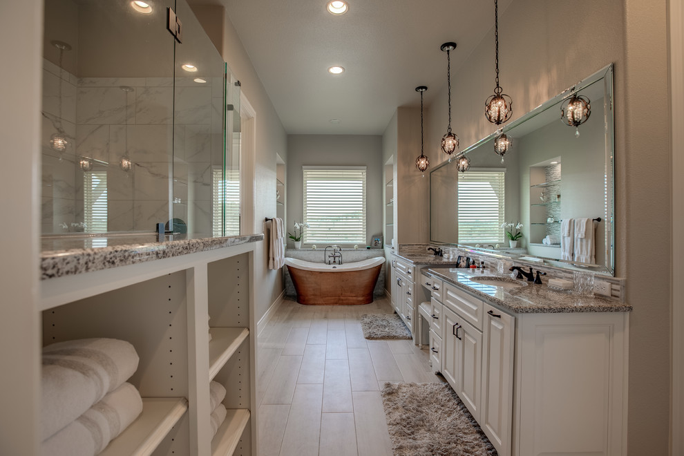Large traditional master bathroom in Austin with raised-panel cabinets, white cabinets, a freestanding tub, an alcove shower, gray tile, marble, beige walls, an undermount sink, granite benchtops, beige floor, a hinged shower door and grey benchtops.