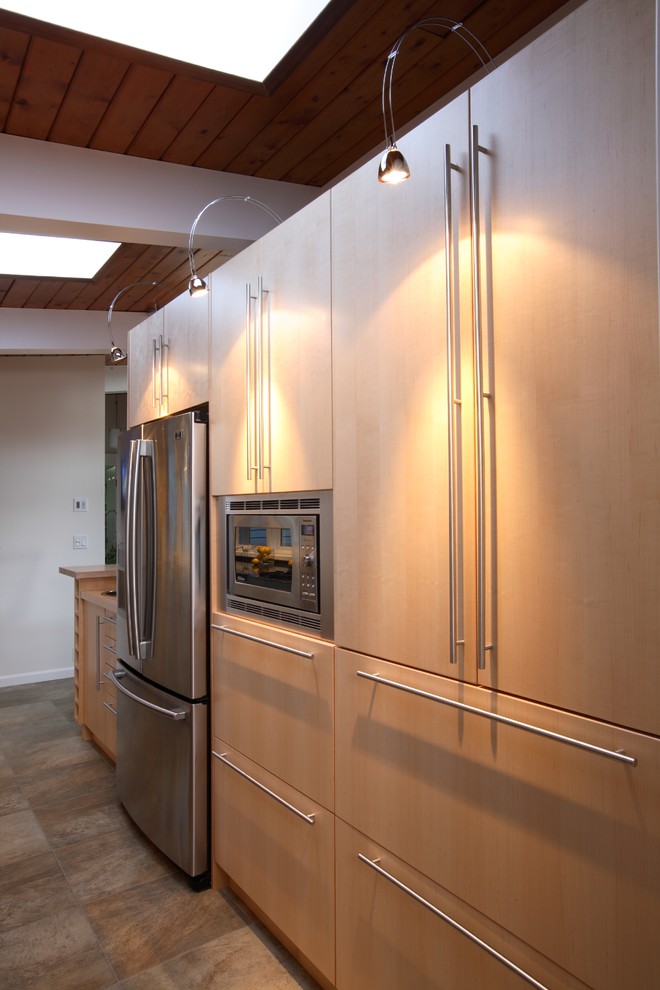 This is an example of a contemporary galley eat-in kitchen in Vancouver with flat-panel cabinets, light wood cabinets and stainless steel appliances.