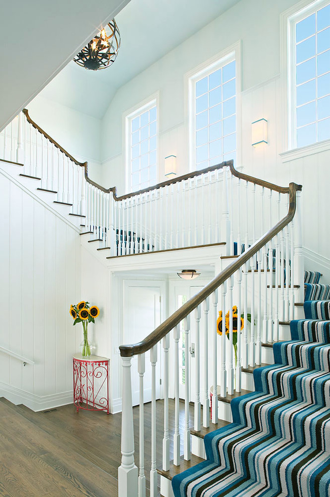 Large traditional carpeted u-shaped staircase in New York with carpet risers and wood railing.