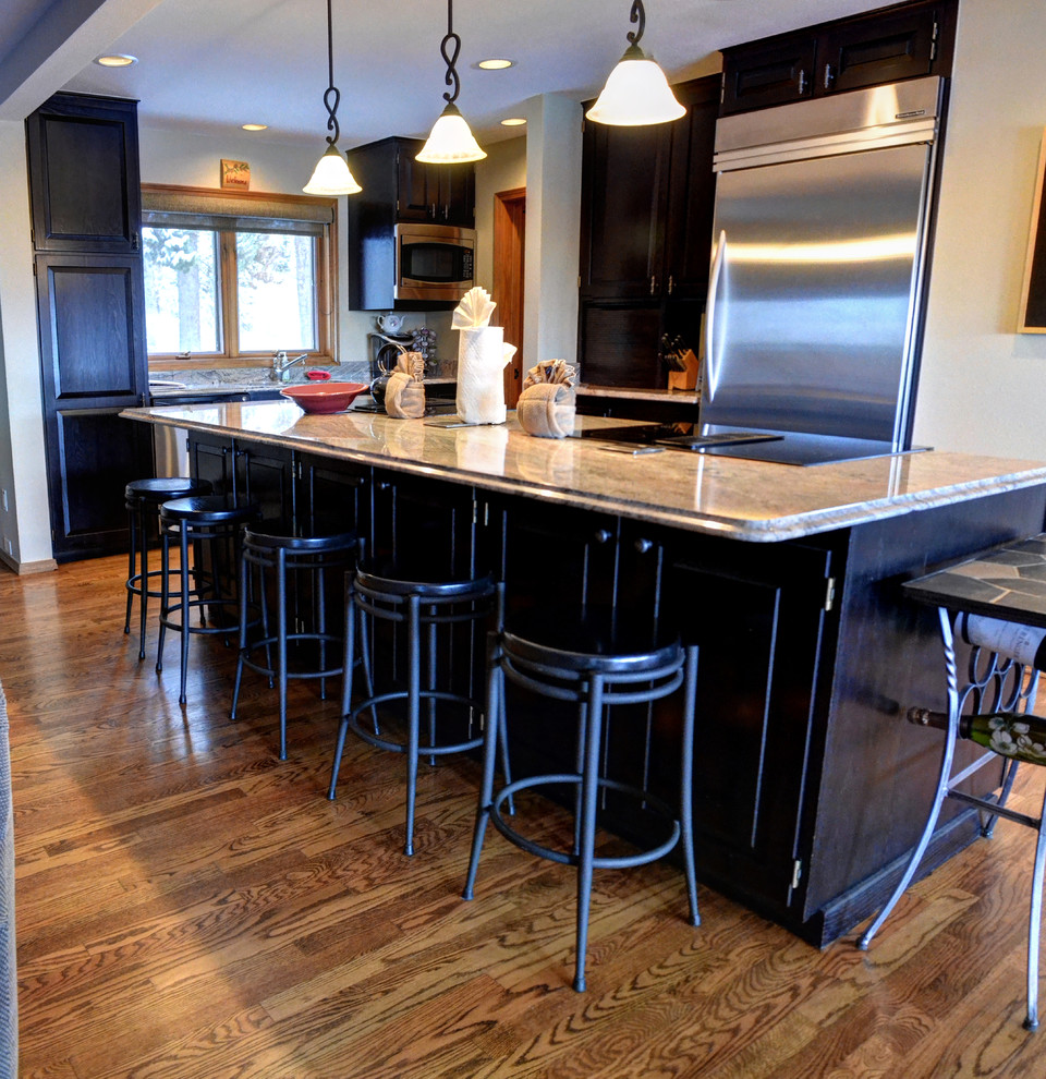Eat-in kitchen - mid-sized transitional l-shaped medium tone wood floor and brown floor eat-in kitchen idea with recessed-panel cabinets, dark wood cabinets, granite countertops, beige backsplash, stainless steel appliances and an island