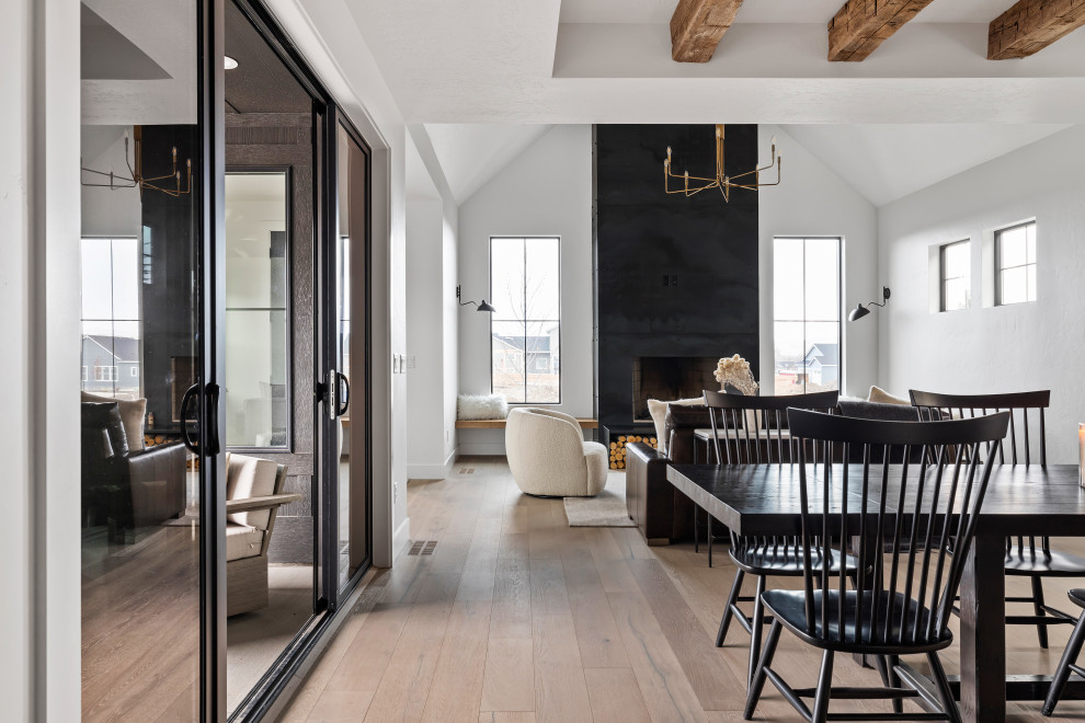 Diseño de comedor escandinavo de tamaño medio abierto con paredes blancas, suelo de madera clara, estufa de leña, marco de chimenea de metal, suelo beige y vigas vistas