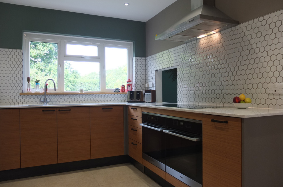 Mid-sized midcentury l-shaped eat-in kitchen in Oxfordshire with a double-bowl sink, flat-panel cabinets, medium wood cabinets, quartzite benchtops, white splashback, ceramic splashback, panelled appliances, ceramic floors, beige floor and white benchtop.