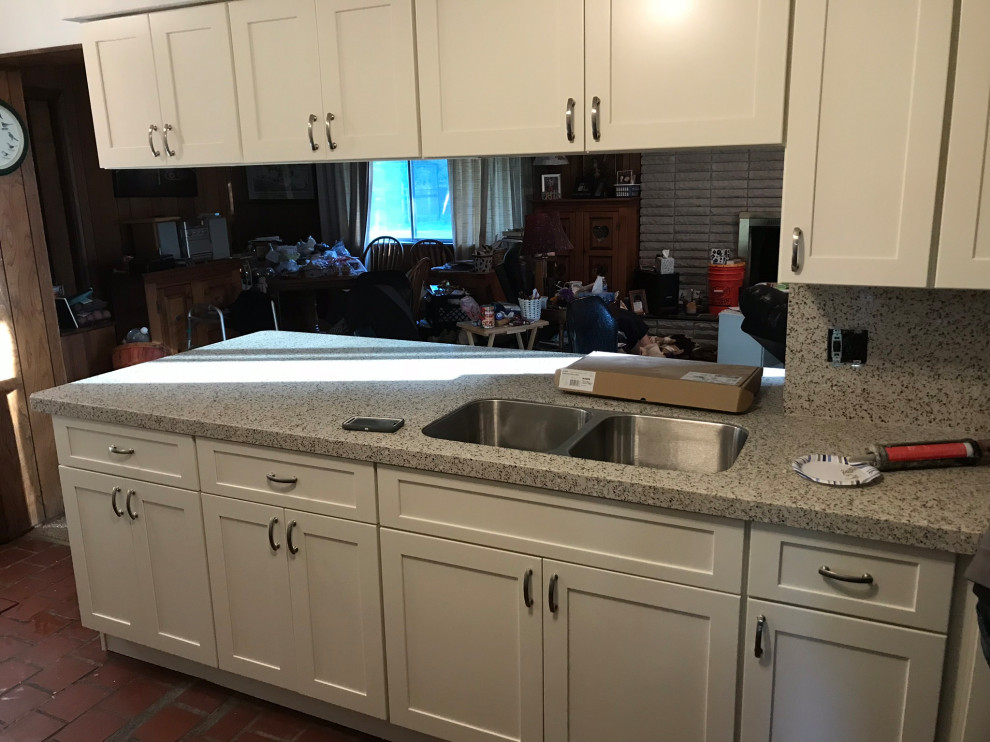 This is an example of a mid-sized modern l-shaped eat-in kitchen in Detroit with a double-bowl sink, shaker cabinets, white cabinets, quartz benchtops, grey splashback, engineered quartz splashback, stainless steel appliances, brick floors, red floor and grey benchtop.