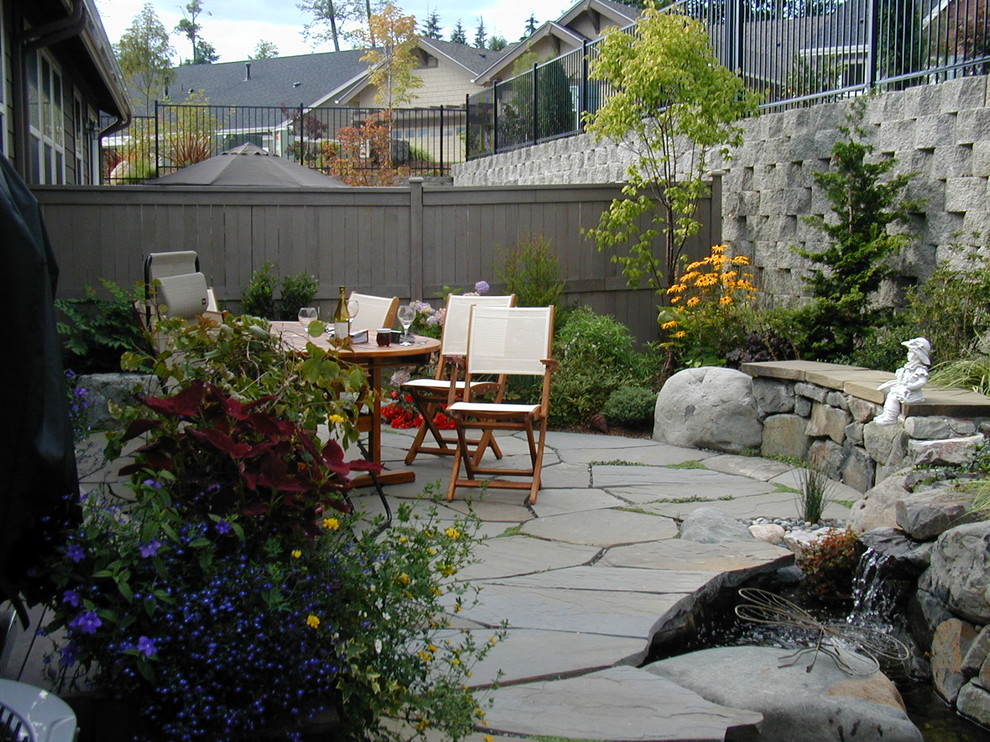 This is an example of a mid-sized traditional backyard full sun formal garden for summer in Seattle with a retaining wall and natural stone pavers.