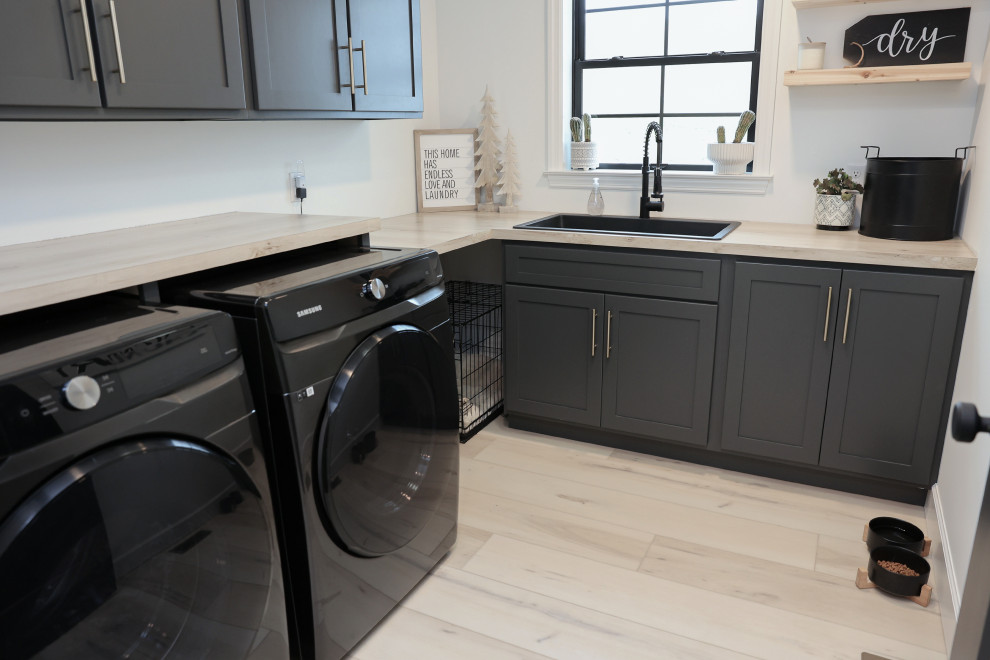 Large modern l-shaped dedicated laundry room in Philadelphia with a drop-in sink, beaded inset cabinets, black cabinets, marble benchtops, white splashback, white walls, vinyl floors, a side-by-side washer and dryer, beige floor and beige benchtop.