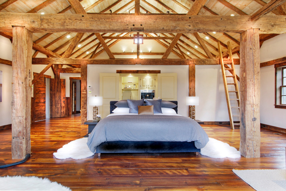 Réalisation d'une très grande chambre parentale chalet en bois avec un mur blanc, un sol en bois brun et un plafond voûté.