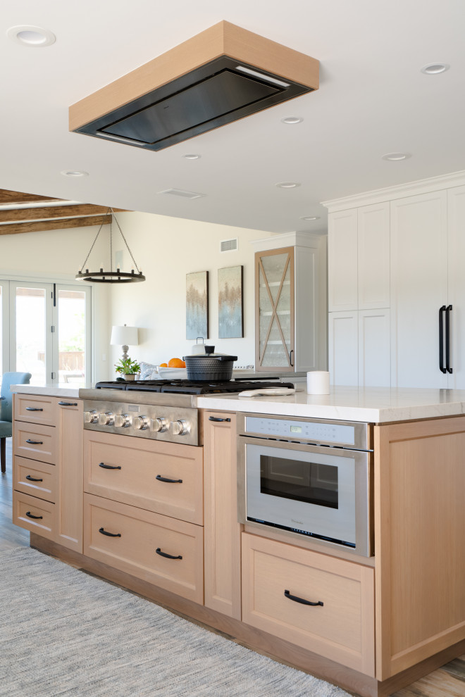 Photo of an expansive farmhouse galley open plan kitchen in San Diego with a belfast sink, recessed-panel cabinets, light wood cabinets, quartz worktops, beige splashback, ceramic splashback, stainless steel appliances, porcelain flooring, an island, brown floors, white worktops and exposed beams.