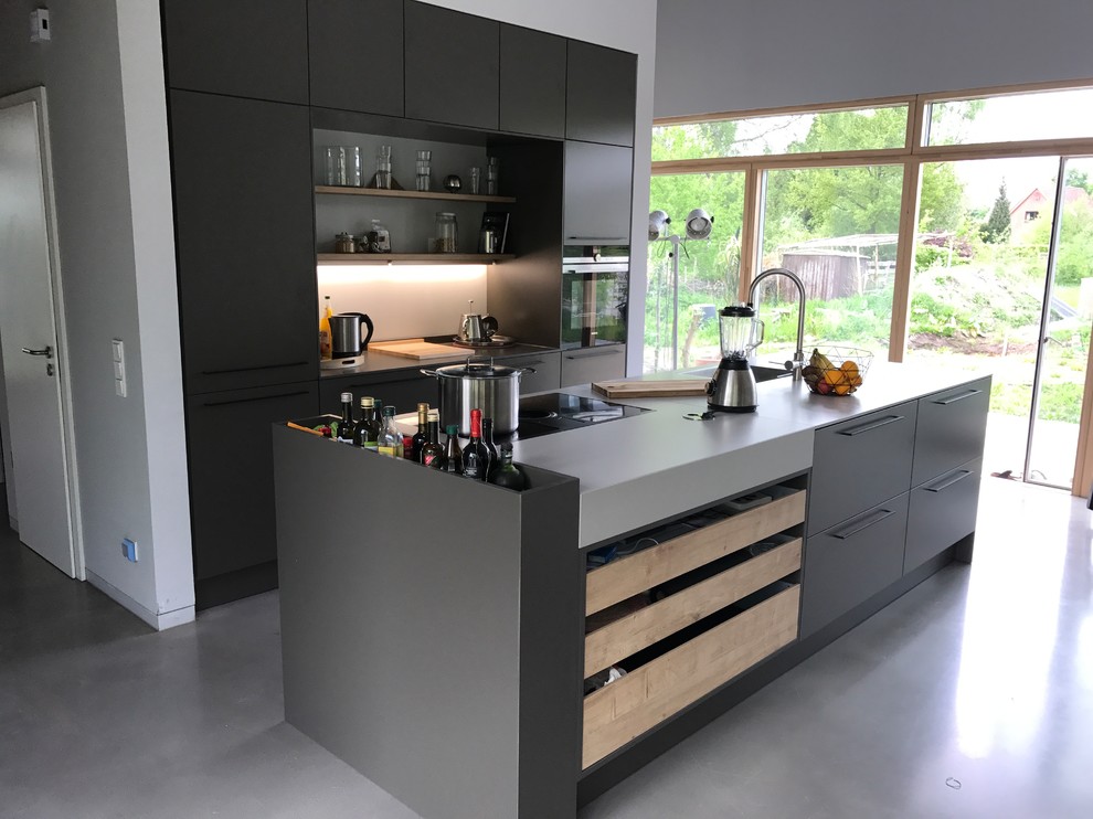 Inspiration for an expansive industrial galley eat-in kitchen in Other with an integrated sink, flat-panel cabinets, grey cabinets, concrete benchtops, white splashback, black appliances, concrete floors, with island, grey floor and grey benchtop.