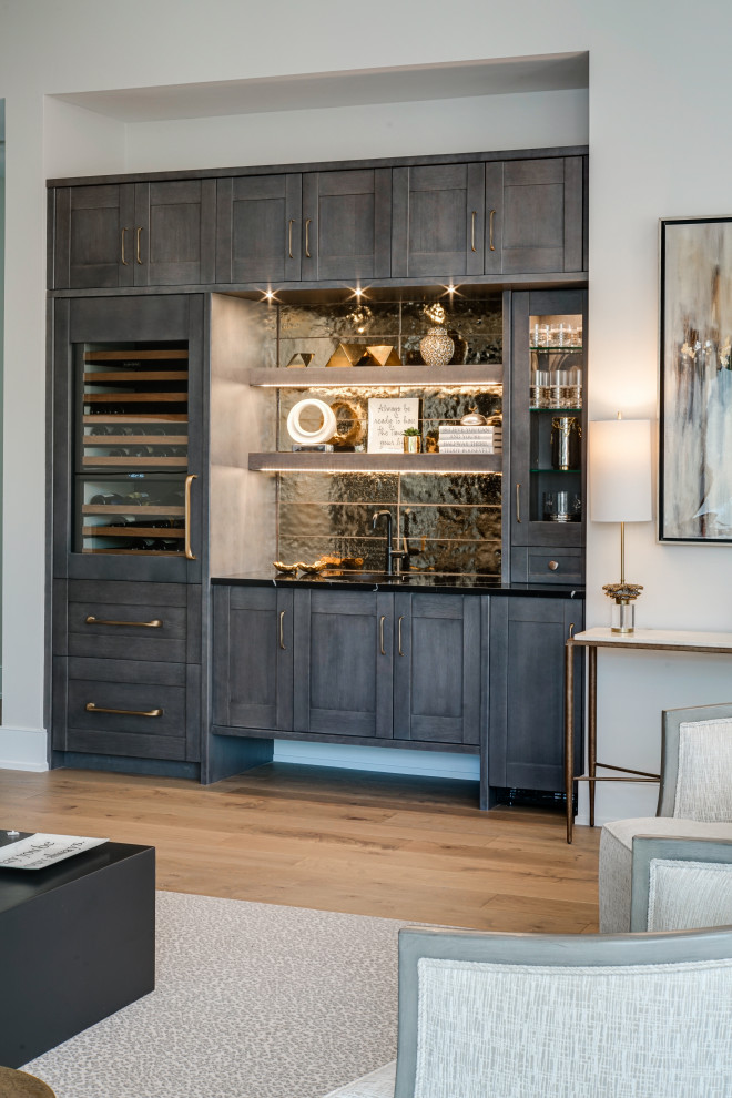 Inspiration for a large contemporary wet bar in Chicago with shaker cabinets, grey cabinets, black splashback, medium hardwood floors, brown floor and black benchtop.