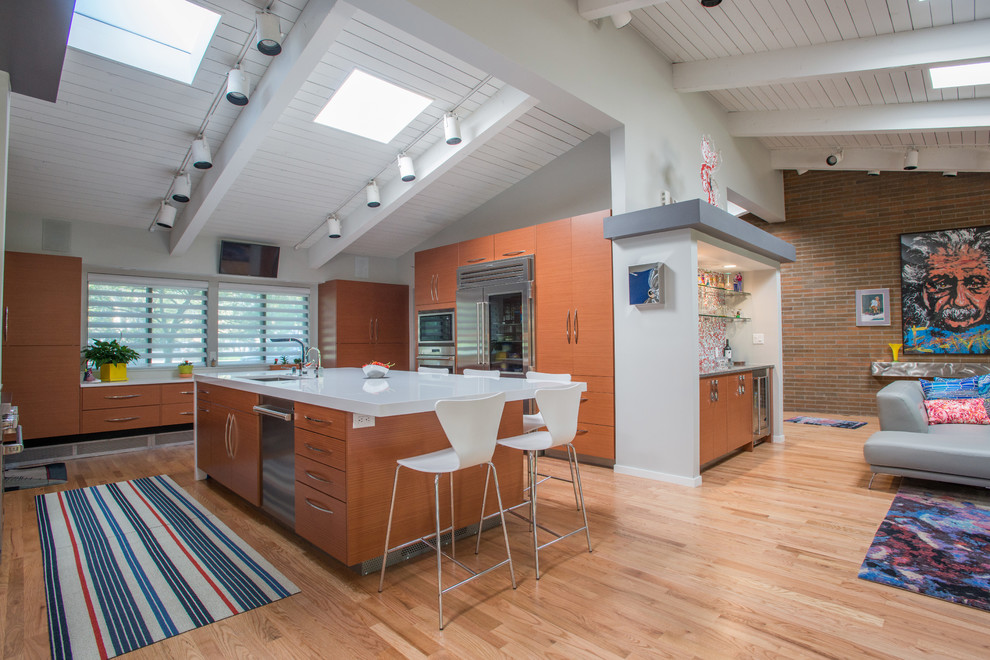 Midcentury open plan kitchen in Denver with an undermount sink, flat-panel cabinets, window splashback, stainless steel appliances, light hardwood floors and with island.