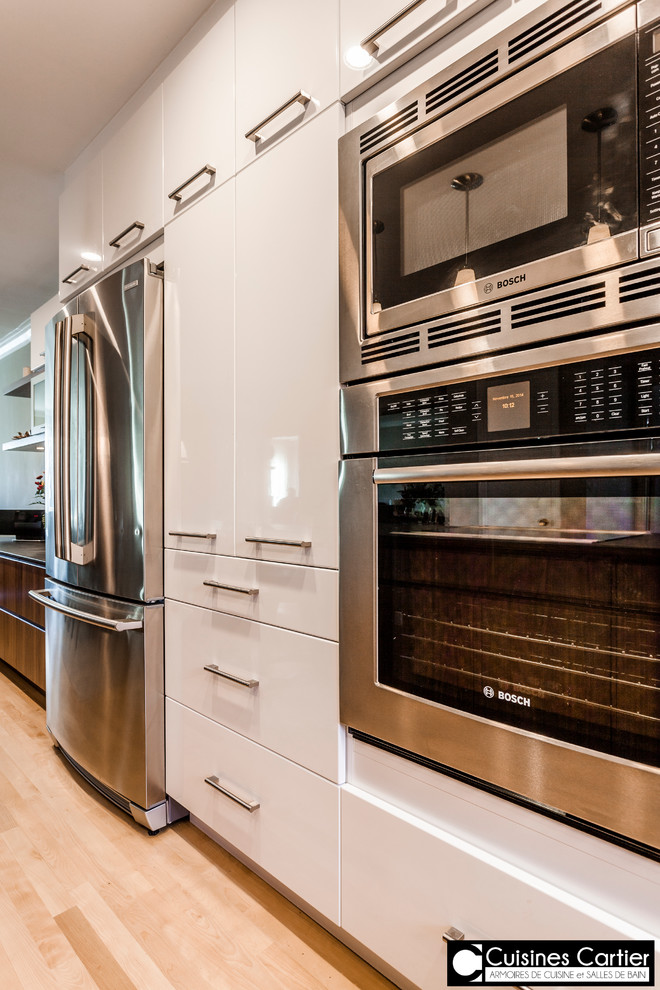 Example of a large transitional galley medium tone wood floor eat-in kitchen design in Montreal with an undermount sink, flat-panel cabinets, dark wood cabinets, quartzite countertops, white backsplash, mosaic tile backsplash, stainless steel appliances and an island