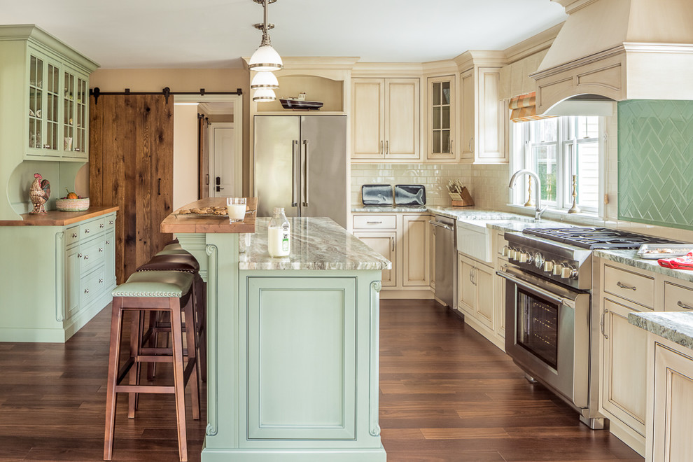 Traditional u-shaped separate kitchen in Portland Maine with with island, a farmhouse sink, beaded inset cabinets, beige cabinets, green splashback, glass tile splashback, stainless steel appliances, medium hardwood floors and brown floor.