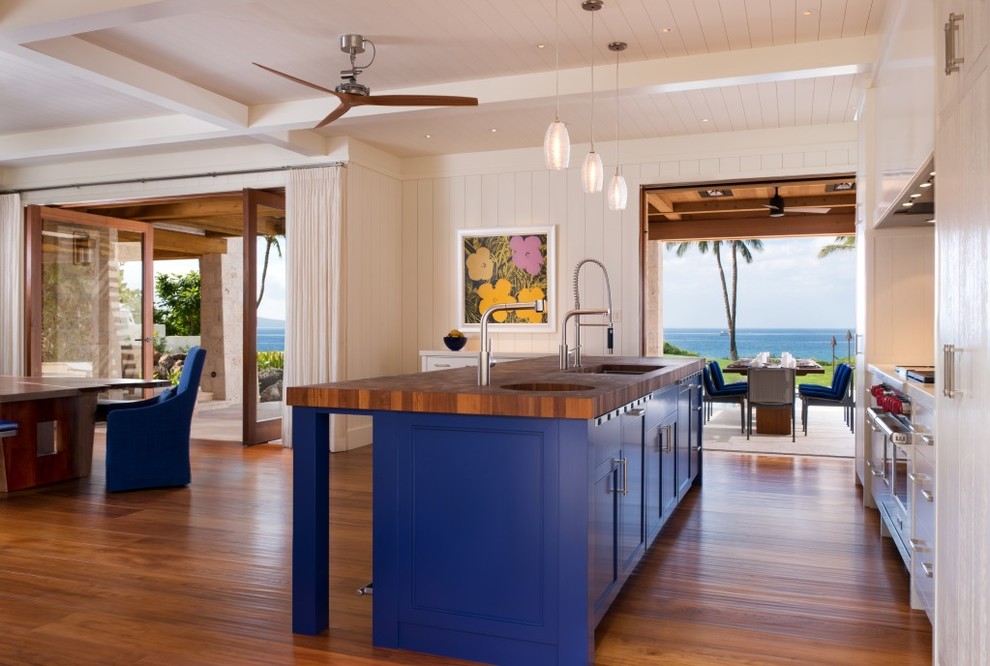 This is an example of a mid-sized tropical galley eat-in kitchen in Hawaii with an undermount sink, flat-panel cabinets, white cabinets, wood benchtops, subway tile splashback, medium hardwood floors, with island, beige splashback, stainless steel appliances and brown floor.