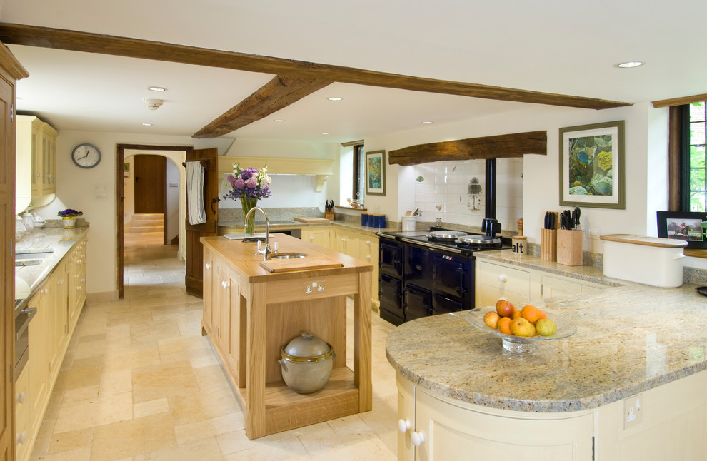 Design ideas for a country u-shaped kitchen in Hampshire with an undermount sink, shaker cabinets, yellow cabinets, white splashback, ceramic splashback, limestone floors, with island and black appliances.