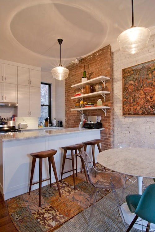 This is an example of a small eclectic galley eat-in kitchen in New York with an undermount sink, shaker cabinets, white cabinets, marble benchtops, white splashback, subway tile splashback, white appliances, medium hardwood floors, with island and brown floor.