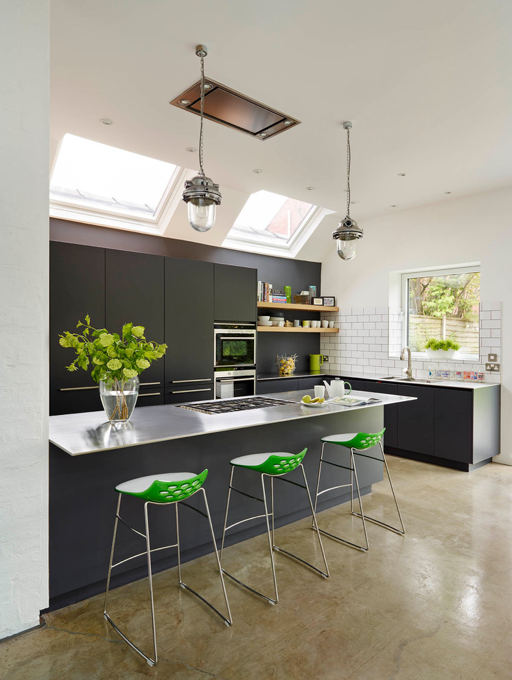 Photo of a large contemporary l-shaped kitchen in London with flat-panel cabinets, black cabinets, stainless steel benchtops, white splashback, concrete floors, beige floor, a double-bowl sink, subway tile splashback, stainless steel appliances and a peninsula.