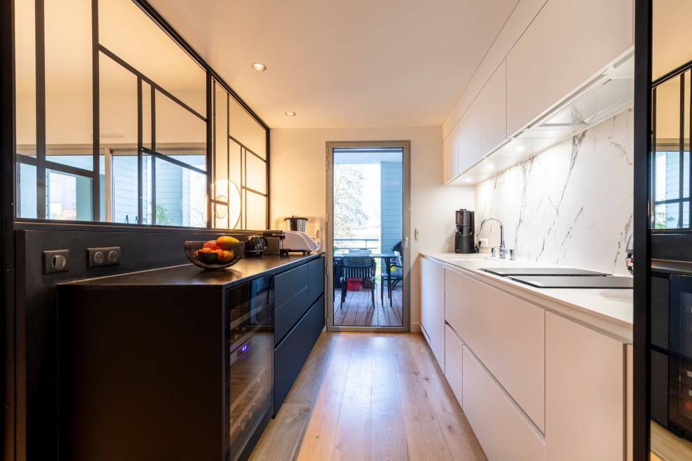 Geschlossene, Zweizeilige Moderne Küche mit Küchenrückwand in Weiß, braunem Holzboden und schwarzer Arbeitsplatte in Nantes