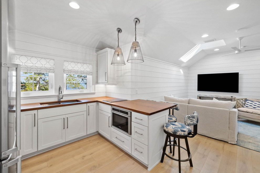 Photo of a small beach style u-shaped kitchen in Other with an undermount sink, shaker cabinets, white cabinets, wood benchtops, stainless steel appliances, light hardwood floors, brown benchtop and vaulted.
