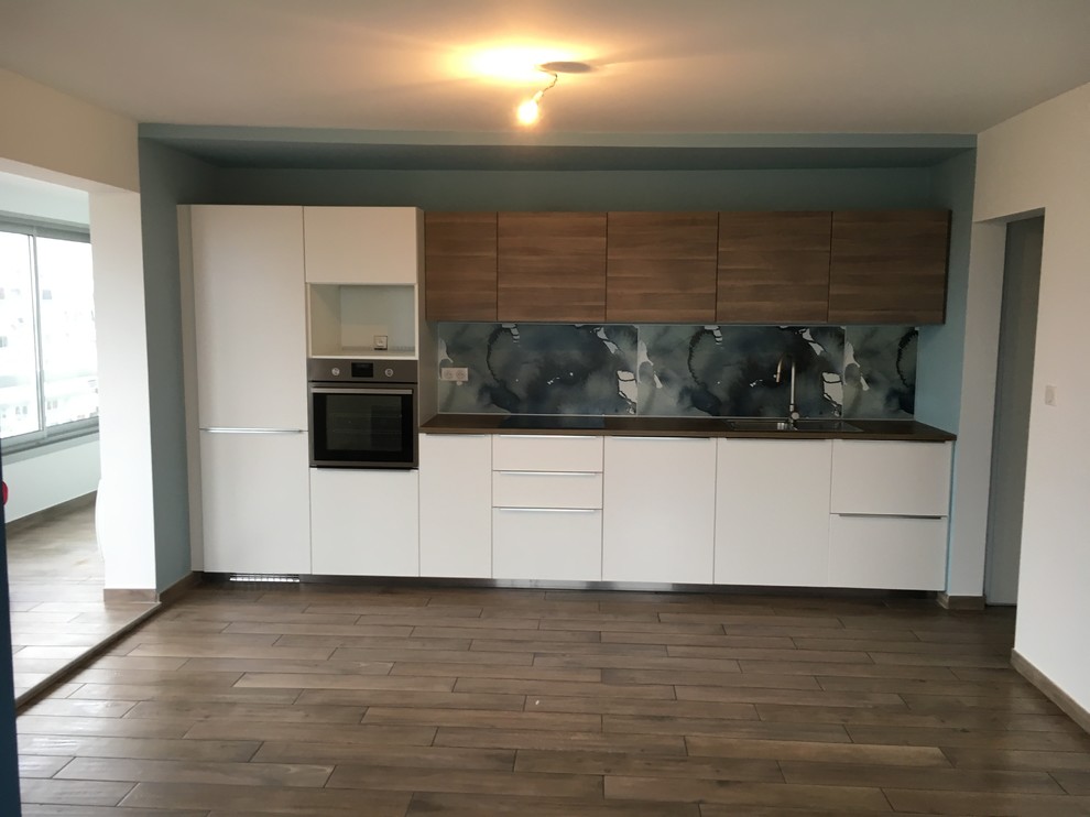 Mid-sized contemporary single-wall eat-in kitchen in Montpellier with a single-bowl sink, beaded inset cabinets, white cabinets, wood benchtops, blue splashback, stainless steel appliances, medium hardwood floors and no island.
