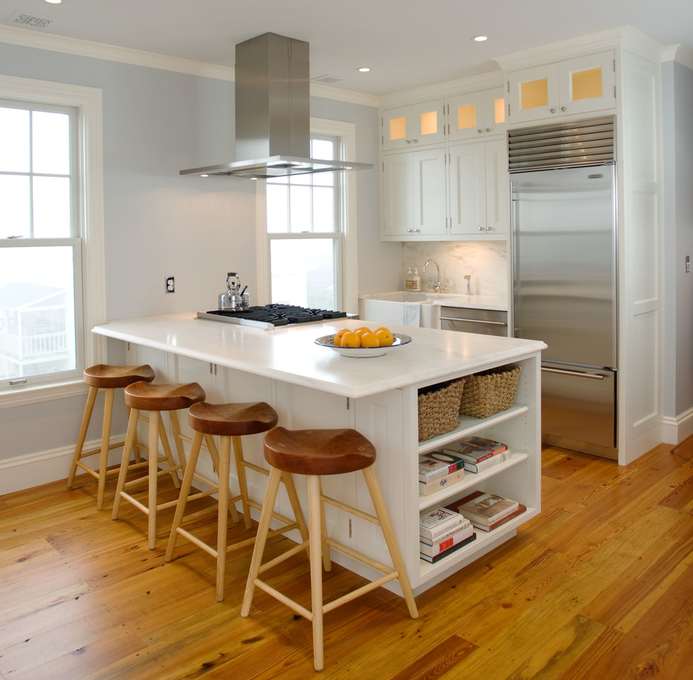 Small traditional galley kitchen in Portland Maine with a farmhouse sink, white splashback, stone slab splashback, stainless steel appliances, medium hardwood floors and a peninsula.
