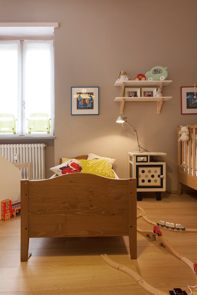 This is an example of an expansive contemporary gender-neutral kids' bedroom for kids 4-10 years old in Turin with beige walls and medium hardwood floors.