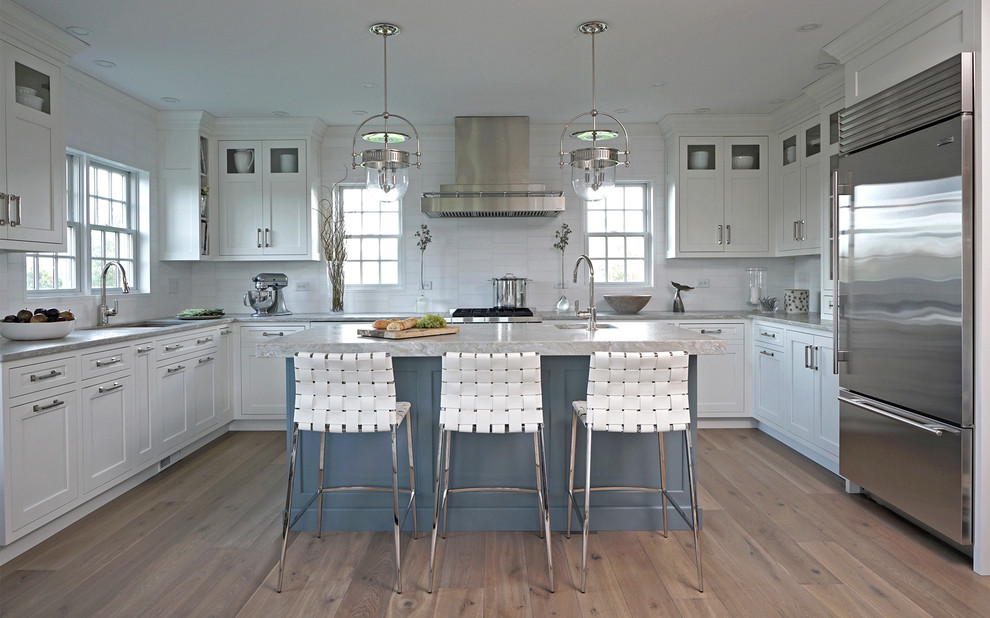 This is an example of a beach style u-shaped kitchen in Boston with an undermount sink, white cabinets, quartzite benchtops, white splashback, stainless steel appliances, light hardwood floors, with island, grey benchtop, recessed-panel cabinets and beige floor.