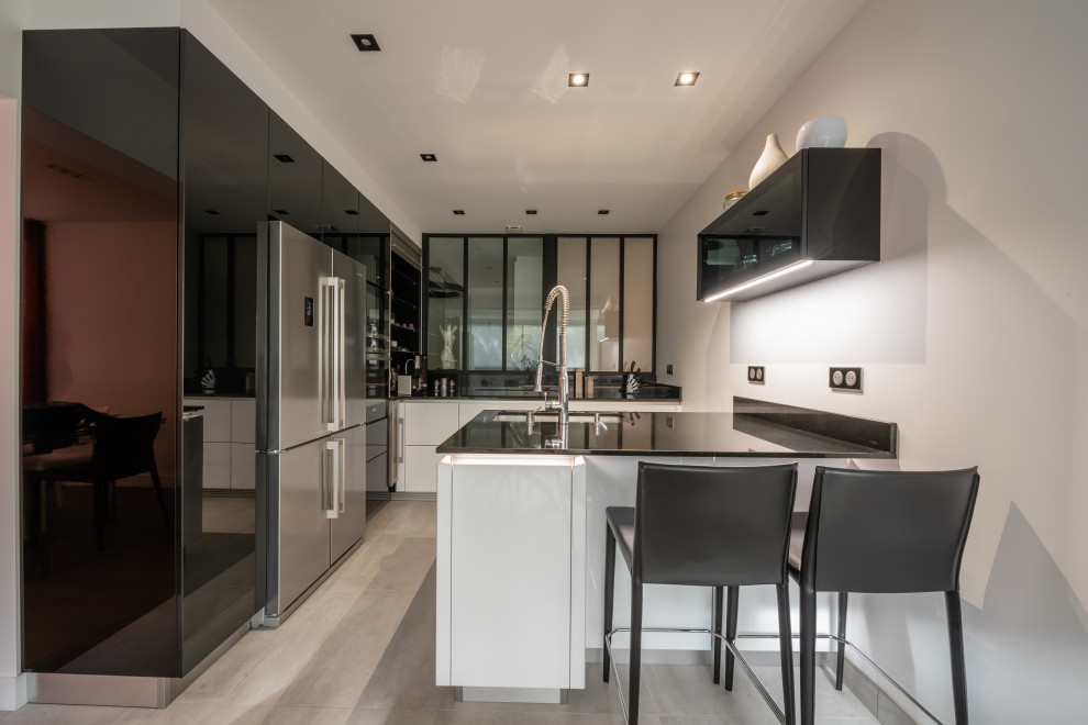 This is an example of a contemporary kitchen in Paris with flat-panel cabinets, black cabinets, a peninsula, an undermount sink, stainless steel appliances, grey floor and black benchtop.
