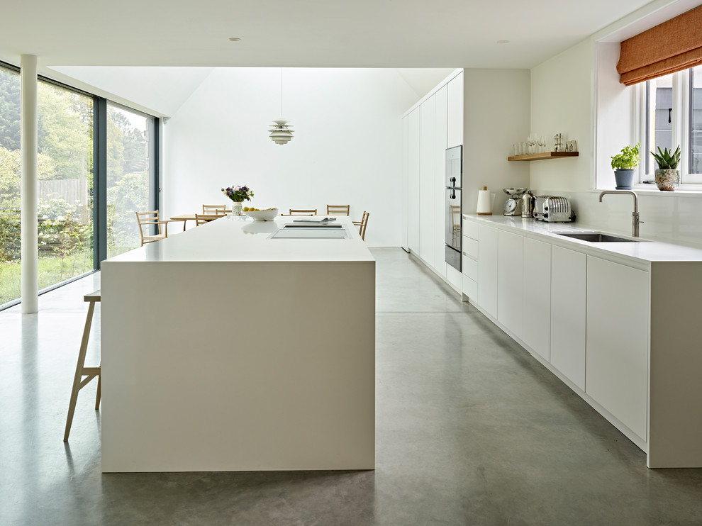Design ideas for a medium sized scandi single-wall kitchen/diner in Kent with a submerged sink, flat-panel cabinets, white cabinets, composite countertops, white splashback, stainless steel appliances, concrete flooring, an island, grey floors and white worktops.