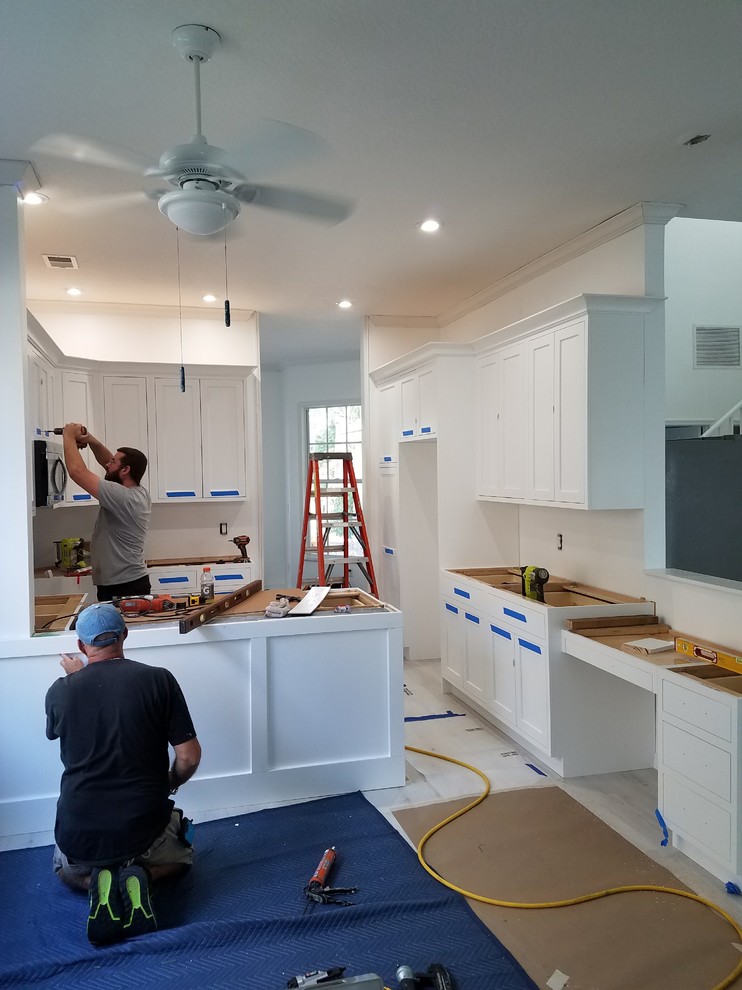 Example of a mid-sized transitional u-shaped laminate floor and white floor kitchen design in Miami with a farmhouse sink, flat-panel cabinets, white cabinets, marble countertops, white backsplash, cement tile backsplash, stainless steel appliances, an island and white countertops