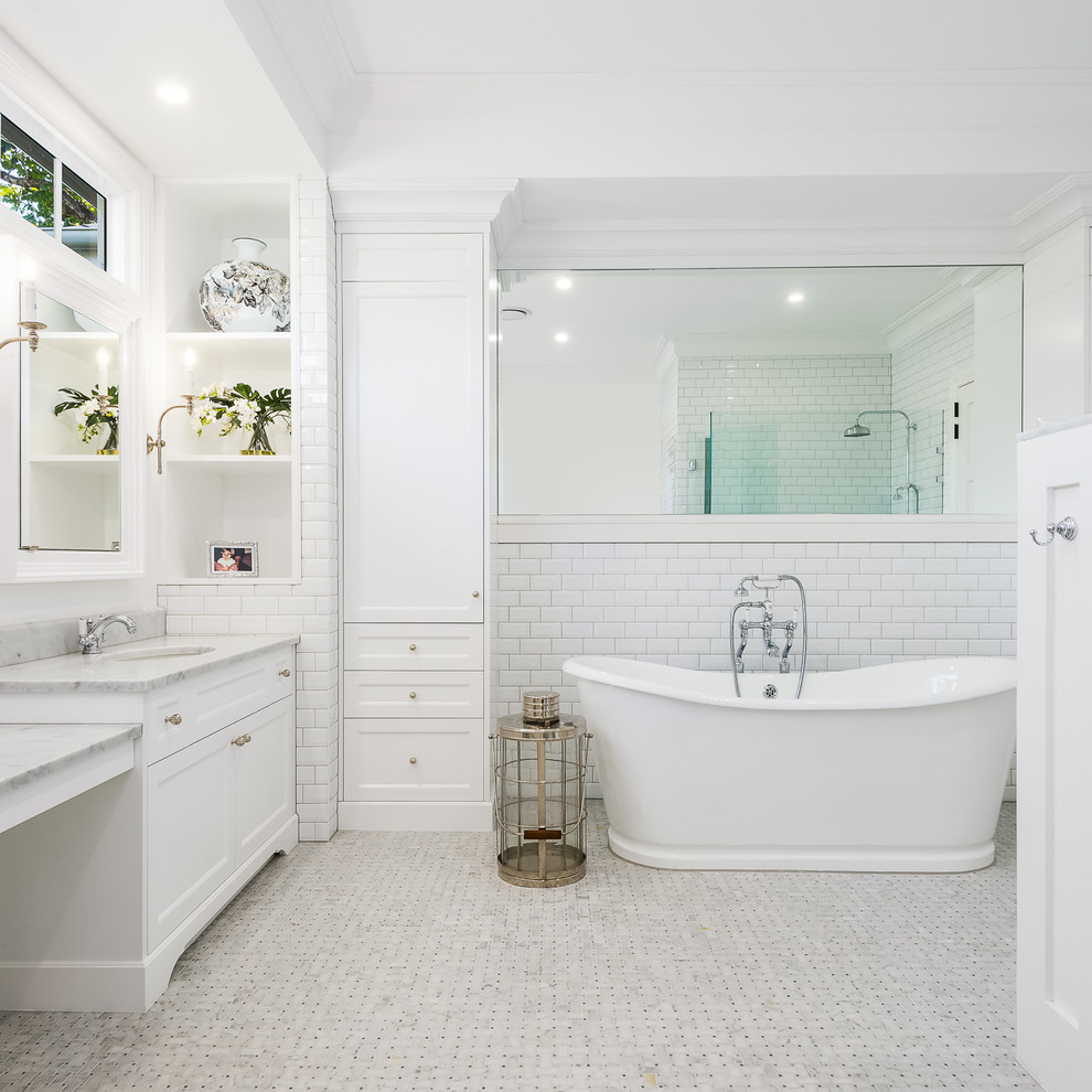 Beach style master bathroom in Gold Coast - Tweed with recessed-panel cabinets, white cabinets, a freestanding tub, a corner shower, white tile, subway tile, white walls, mosaic tile floors, an undermount sink, marble benchtops, white floor, a hinged shower door and grey benchtops.