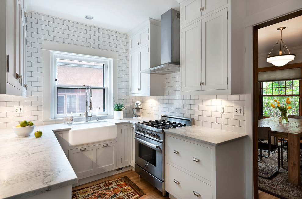 Design ideas for a traditional l-shaped separate kitchen in Denver with a farmhouse sink, shaker cabinets, white cabinets, marble benchtops, white splashback, subway tile splashback, stainless steel appliances and light hardwood floors.