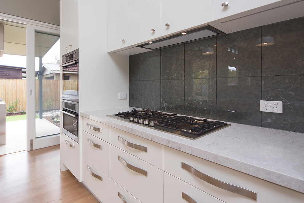 Design ideas for a mid-sized contemporary galley eat-in kitchen in Brisbane with a drop-in sink, flat-panel cabinets, white cabinets, quartz benchtops, green splashback, glass tile splashback, stainless steel appliances, medium hardwood floors and with island.
