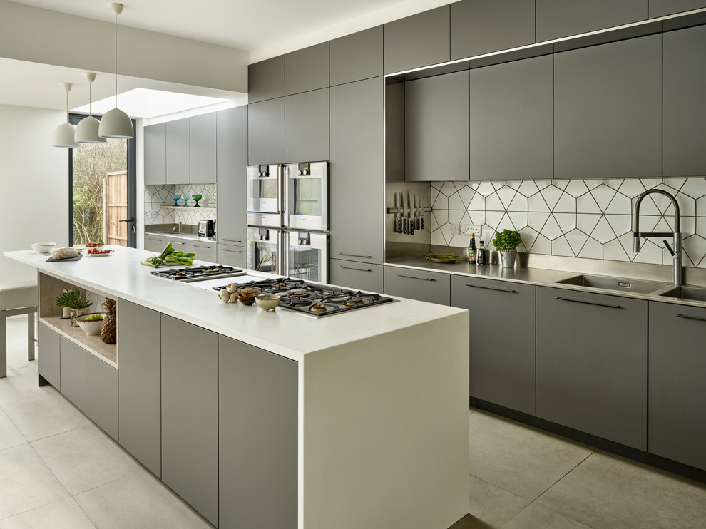 Contemporary open plan kitchen in London with an integrated sink, flat-panel cabinets, grey cabinets, solid surface benchtops, white splashback, ceramic splashback, stainless steel appliances, ceramic floors, with island and grey floor.