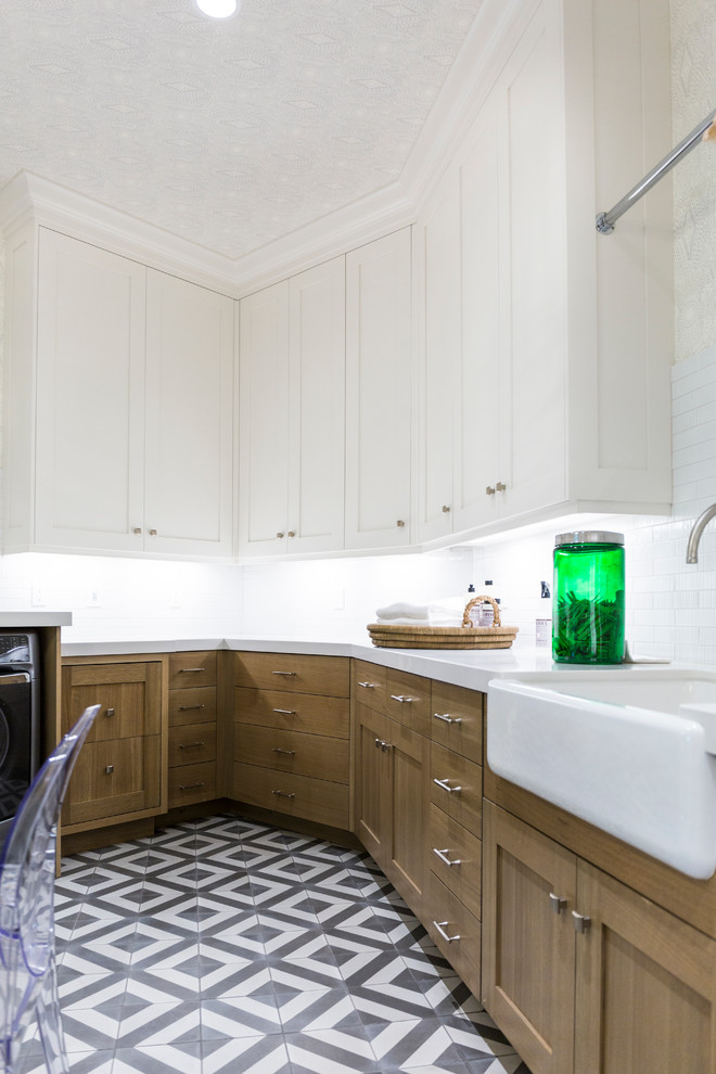 This is an example of a large transitional u-shaped laundry room in Salt Lake City with a farmhouse sink, shaker cabinets, white cabinets, marble benchtops, grey splashback, beige walls, marble floors, a side-by-side washer and dryer, multi-coloured floor and black benchtop.