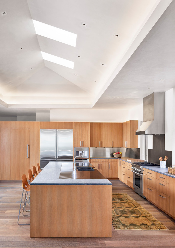 Design ideas for an expansive midcentury l-shaped open plan kitchen in Austin with a double-bowl sink, flat-panel cabinets, light wood cabinets, grey splashback, stainless steel appliances, dark hardwood floors, with island, brown floor and grey benchtop.