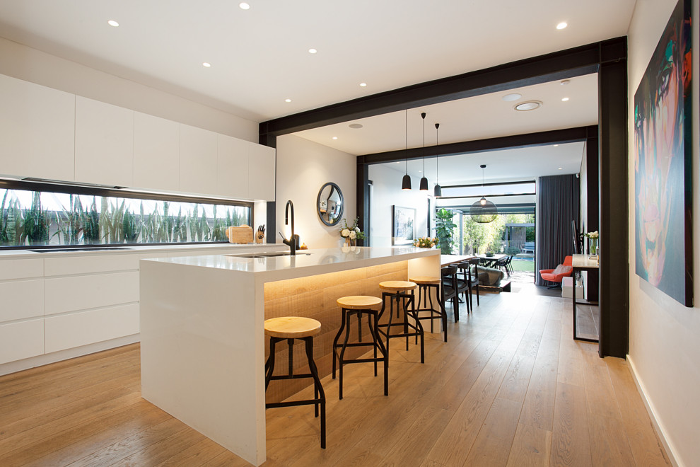 Photo of a mid-sized contemporary u-shaped eat-in kitchen in Sydney with a double-bowl sink, recessed-panel cabinets, white cabinets, quartz benchtops, grey splashback, window splashback, stainless steel appliances, medium hardwood floors, with island, brown floor and white benchtop.