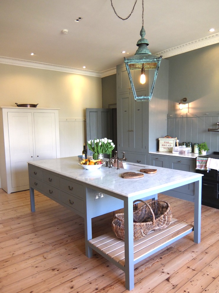 Design ideas for an expansive country kitchen in London with a farmhouse sink, grey cabinets, grey splashback, light hardwood floors, with island, shaker cabinets, marble benchtops and black appliances.